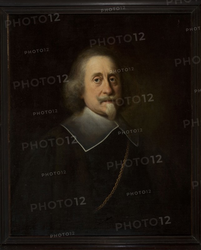 Man with a white Spanish beard; unknown painter; 1640–1660; portrait; height 79.0 cm, width 64.6 cm also listed as 79 × 64.5 cm., A framed oil portrait of an older man shown from the chest up against a dark background, with pale skin and light gray hair that is wavy and shoulder-length; he has a small pale beard and mustache. He wears a dark garment with a broad white collar edged in a thin dark line, and a gold chain draped across his chest. The overall color palette includes dark brown and black tones in the background and clothing, pale beige and pink in the face and beard, white in the collar, and gold in the chain, with the frame appearing dark brown.