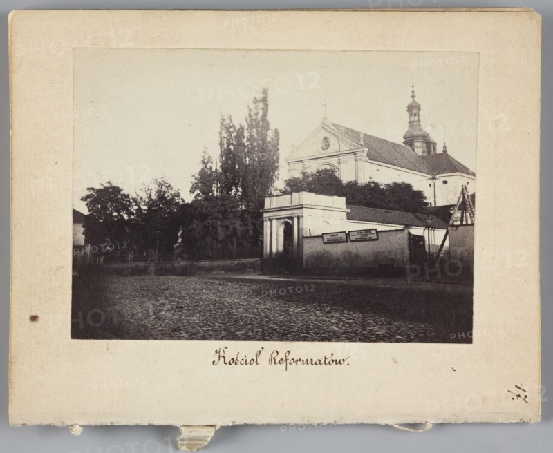 Warsaw. Reformati Church St. Anthony of Padua Church at Senatorska Street, Beyer, Karol 1818-1877 photographer, pavement, signs, Warsaw Masovian Voivodeship, St. Anthony of Padua Church Warsaw ; Sródmiescie, Reformati Church Warsaw, Senatorska Street Warsaw ; street, 1861 - 1863, Warsaw place of creation, photograph, nature photograph, photographic print: height 6.2 cm, width 8.6 cm, backing: height 11.3 cm, width 8.8 cm, A sepia-toned photograph mounted on a beige card shows a street scene with a group of trees and a building complex dominated by a church with a triangular pediment and a domed tower, visible behind a lower wall and gateway; the foreground is a cobblestone street leading toward the entrance, and there are a few signs mounted on the wall near the gateway; colors visible include shades of brown, beige, black, and off-white.