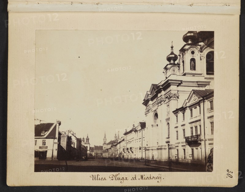 Dluga Street from Miodowa Street View towards Freta Street, Karol Beyer 1818–1877 photographer, 1861–1863, photograph from nature; photographic print: image 7 × 8.8 cm; support 11.4 × 8.8 cm. Depicts Warsaw: Dluga Dluga Street, Freta Freta Street, Pauline Church Freta Street, St. Jacek Church Freta Street, Piarist Church Dluga Street, Holy Trinity Dluga Street, Orthodox churches., A sepia-toned street scene showing a wide street flanked by buildings, with a large ornate building on the right featuring domed towers, decorative facades, arched windows, and a small balcony, and a row of smaller buildings receding into the distance on the left; the sky appears pale, and the foreground street area is darker, with a few indistinct figures and shadows near the buildings. Colors visible include sepia/brown tones, beige, cream, black, and pale off-white.