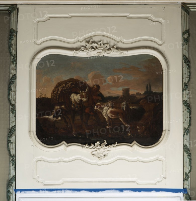 Shepherd's Scene with a Laden Donkey, Roos, Philipp Peter 1657–1706 painter. General tones of brown against a grey-blue sky with pink clouds and a slightly marked mountain range. The middle distance on the right shows buildings and clumps of trees. The foreground is a genre scene: beside a donkey laden with baskets a peasant secures the load; nearby are two dogs, two goats, and two rams. 18th century, Italy; overdoor. Height 92.0 cm, width 127.5 cm., A framed painting set into an ornate white wall panel shows a pastoral scene with a group of animals and a person interacting outdoors under a cloudy sky. The painting contains a large pack animal with a woven load, several dogs or similar animals nearby, and a person leaning toward the animals. The background of the painting includes distant landscape features and a sky with clouds. The surrounding panel is cream to off-white with decorative moldings and sculpted floral motifs, and the vertical edges beside the panel show carved elements ...
