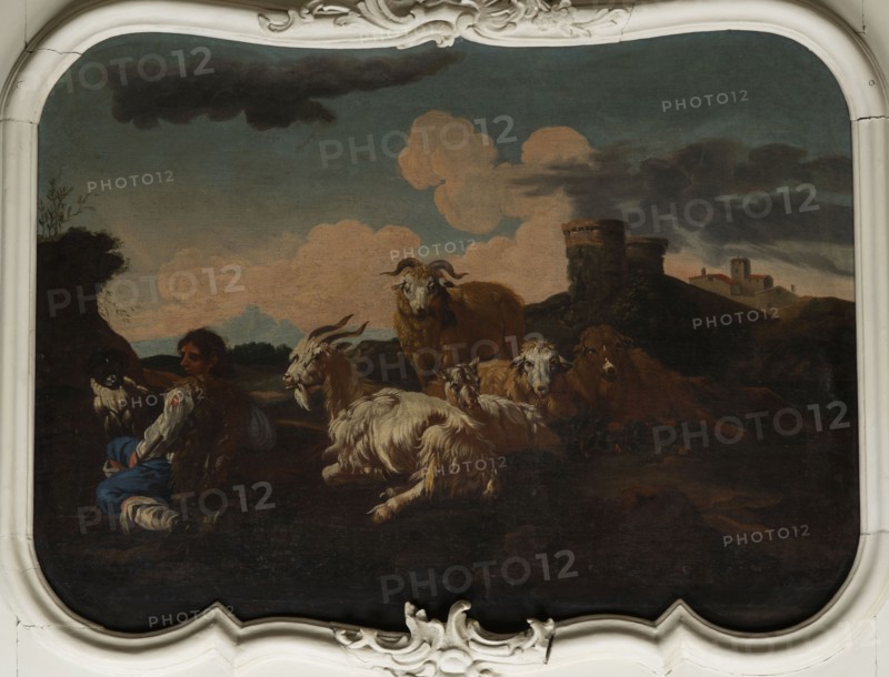 Shepherd Scene with a View of the Castle, Roos, Philipp Peter 1657–1706 painter. Multicolored composition with dominant shades of brown against a blue sky with white clouds and a distinct pink glow. In the foreground, the central group consists of two goats, a male and a female, lying down, with a male goat standing behind them. On the left, a slope, a dog, and a shepherd sitting in half-profile, wearing a brown sheepskin coat, blue trousers, a white shirt, and stockings. On the right, in the background on a hill, two cylindrical buildings, behind them castle buildings. 18th century, Italy; overdoor. Height 92.0 cm, width 115.0 cm., A pastoral scene shows a group of animals and a seated person in a landscape under a sky with large clouds; the animals include several goats with shaggy white and brown fur and a larger brown sheep or ram with curved horns, all gathered on dark ground; the seated person wears garments in blue and white with a darker vest and is positioned near the animals;...