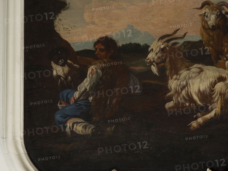 Shepherd Scene with a View of the Castle, Roos, Philipp Peter 1657–1706. Multicolored composition with dominant shades of brown against a blue sky with white clouds and a distinct pink glow. In the foreground, the central group consists of two goats, a male and a female, lying down, with a male goat standing behind them. On the left, a slope, a dog, and a shepherd sitting in half-profile, wearing a brown sheepskin coat, blue trousers, a white shirt, and stockings. On the right, in the background on a hill, two cylindrical buildings and behind them castle buildings. 18th century, Italy; overdoor; height 92.0 cm, width 115.0 cm., A dark-toned painting fragment showing a seated person with brown hair wearing a white-sleeved garment, a brown fur-like vest, and blue trousers, positioned near a group of goats; one goat with long curved horns and shaggy white and beige fur faces toward the seated figure, another goat with similar coloring lies nearby, and a darker-faced goat with lighter fur ...