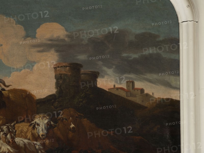 Shepherd Scene with a View of the Castle, Roos, Philipp Peter 1657–1706 painter. Multicolored composition with dominant shades of brown against a blue sky with white clouds and a distinct pink glow. In the foreground, the central group consists of two goats, a male and a female, lying down, with a male goat standing behind them. On the left, a slope, a dog, and a shepherd sitting in half-profile, wearing a brown sheepskin coat, blue trousers, a white shirt, and stockings. On the right, in the background on a hill, two cylindrical buildings with castle buildings behind them. 18th century, Italy; overdoor; height 92.0 cm, width 115.0 cm., A painted scene showing a group of animals in the foreground including several sheep with white and brown wool and a brown cow, positioned before a dark, rocky hill topped by two round stone towers. Behind the hill there is a cluster of small buildings with red roofs and pale walls and a taller square tower among them. The sky above contains large pale ...