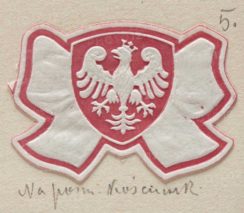 Lowicz. World War I period prints, charity, Poland, wars, Lowicz Lódz Voivodeship, World War I 1914–1918, stamps, 20th century, stamps, A die-cut paper emblem shaped like a bow with a central shield shows an embossed bird with spread wings and a small crown, all in white, set against a red background inside the shield; the bow portion is primarily white with a red outline, and the background behind the emblem is a beige textured paper.