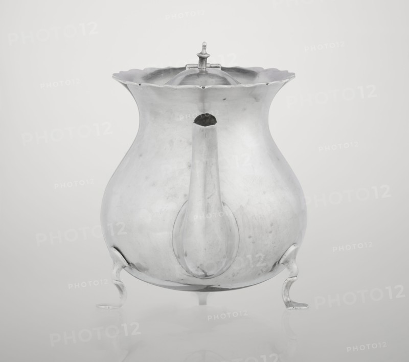 Pear-shaped teapot supported on three legs, smooth, with a flared upper edge topped with a pinnacle, with a spout-shaped spout, on the axis silver bushings for mounting the missing wooden handle. Maker: Stokes & Ireland Ltd Birmingham; goldsmiths; fl. 1872–1925. Inscription/markings: role classification of maker, goldsmiths. Date: 1900/1901. Place of origin: Chester, England, Great Britain. Material/function: vessel tea accessory. Dimensions: height 11.5 cm; width 15.5 cm; depth 10 cm; weight 330 g. Provenance: scrap - purchase, A metallic teapot-like vessel with a bulbous body and a wavy, scalloped rim sits on a smooth surface, shown from the front with a short, rounded spout protruding toward the viewer and a domed lid topped by a small finial; the vessel stands on a group of curved feet and displays a reflective, slightly worn surface in shades of silver and gray against a pale gray background.