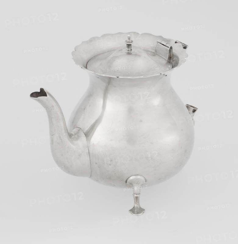 Teapot by Stokes & Ireland Ltd Birmingham; goldsmiths; fl. 1872–1925. Pear-shaped teapot supported on three legs, smooth, with a flared upper edge topped with a pinnacle, with a spout-shaped spout; on the axis are silver bushings for mounting the missing wooden handle. Inscribed/corporate slogans of maker. Made 1900–1901, Chester, England, Great Britain. Vessel. Height 11.5 cm; width 15.5 cm; depth 10 cm; weight 330 g., A rounded metal vessel with a bulbous body and a flared scalloped rim, shown from a slightly elevated angle; it has a curved spout on one side and a hinged lid with a small finial on top, and it stands on a small turned foot. The visible colors are silver and shades of gray on a light gray background.