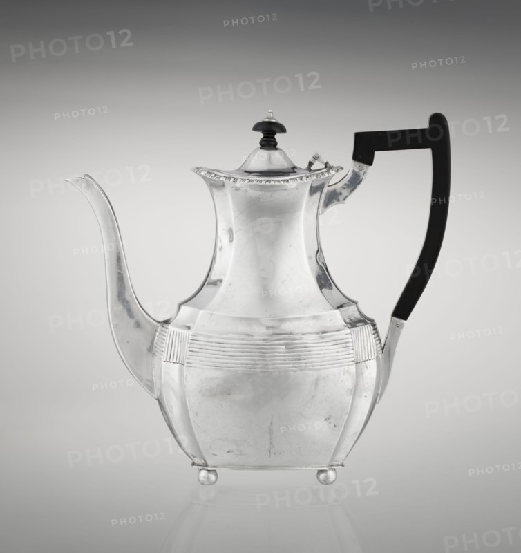 Coffee pot by Harris, CS & Sons London, goldsmiths' firm, fl. 1817–1933 and Harris, Charles Stuart maker, fl. 1852–1897. Scrap-purchased. Pear-shaped, ribbed coffee vessel with godron ornaments; supported on four ball-shaped profiled legs; belly decorated with a band of narrow half-cylinders and grooves. High side spout-like handle and a contemporary wooden axial handle set in silver sockets. Upper edge edged with a godron band; hinged lid domed in the center, topped with a bowling-pin finial. Dated 1895/1896, London, England. Height 21.2 cm; width 18.5 cm; depth 10 cm; weight 640 g., A reflective metal teapot with a curving spout and a high-arched handle is shown against a light gray gradient background; the teapot has a polished silver surface with subtle scratches and scuffs, a domed lid topped with a small dark knob, decorative fluting around the midsection, rounded body panels, and small round feet, and the handle appears dark black while the overall scene includes shades of silve...