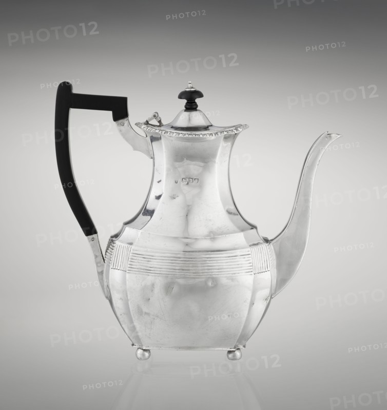 Coffee pot by Harris, CS & Sons London; goldsmiths' firm; fl. 1817–1933 and Harris, Charles Stuart fl. 1852–1897. Scrap-purchased; ribbed, pear-shaped coffee vessel supported on four ball-shaped profiled legs. Belly decorated with a band of narrow half-cylinders and grooves; high spout-like handle to the side and a wooden axial handle contemporarily added set in silver sockets. Upper edge edged with a godron band; hinged lid domed in the center topped with a bowling-pin finial. 1895/1896. London, England. Height 21.2 cm; width 18.5 cm; depth 10 cm; weight 640 g., A reflective metal teapot with a curved spout and a tall, angular body standing on small round feet, featuring a dark handle and a domed lid topped with a small dark finial; the teapot has horizontal ribbed decoration around its midsection and a subtle scalloped rim on the lid, with visible surface scratches and reflections; the background is a smooth gradient from light gray at the center to darker gray toward the edges.