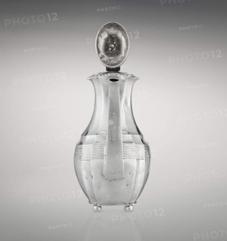 Coffee pot, maker: Harris, CS & Sons London; goldsmiths' firm; fl. 1817–1933 and Harris, Charles Stuart fl. 1852–1897. Purchased, Silver coffee vessel, ribbed, pear-shaped, supported on four ball-shaped profiled legs; belly decorated with a band of narrow half-cylinders and grooves. High spout-like side handle and a contemporary wooden axial handle set in silver sockets. Upper edge edged with a godron band; hinged lid, domed center, topped with a bowling-pin finial. Dated 1895–1896. Place: London, England. Dimensions: height 21.2 cm; width 18.5 cm; depth 10 cm; weight 640 g., A metallic pitcher with a hinged oval lid open upward, showing a reflective inner surface; the pitcher has a tall, slender neck that flares at the rim, a broad handle running down the front, a rounded body with horizontal ribbed bands near the upper section, and rests on a few small rounded feet. Visible colors include silver, gray, and subtle darker gray reflections against a gradient gray background.
