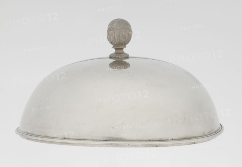Platter lampshade, Scott, Digby & Smith, Benjamin fl. 1802–1807, goldsmith. Silver hemispherical lampshade with a non-original, contemporary handle; smooth surface with a profiled ribbon edge. On the side, a relief plaque with the Czartoryski coat of arms on a paludament, beneath a princely mitre, with labry and the motto Badz co sie Be that as it may. Dated 1803/1804, made in London, England, Great Britain. Vessel; height 8.5 cm, diameter 15.2 cm, weight approx. 230 g., A dome-shaped metal cloche with a rounded finial on top, showing a smooth curved surface with some small scratches and wear; the cloche and finial are metallic grey and silver, with slight darker patina on the finial, and a thin raised rim around the base.