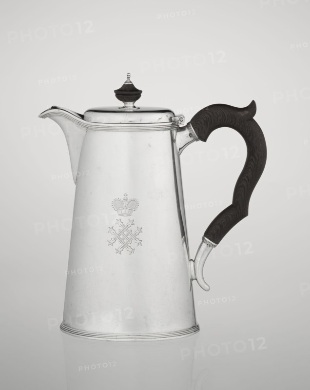 Conical coffee pot with hinged lid, slightly arched and flattened at the top, topped with a wooden handle; short spout; on the axis two sleeves for attaching a wooden handle added contemporarily. On the mantle engraved monogram tied HH beneath a ducal mitre; monograms, rank crowns, ducal mitre heraldry. Maker: Edward Barnard & Sons Ltd., London goldsmiths, fl. ca. 1680– . Also associated makers/sellers: Clark, Alfred Ltd., London goldsmiths and sellers, fl. 1898–1934. Materials: silver; wooden handle made. Function: coffee ware. Date inscription: 1890/1891. Place: London, England, Great Britain. Dimensions: height 17.3 cm, width 11 cm, depth 8.4 cm; weight 627 g., A tall metallic pitcher with a reflective silver surface and a dark wooden curved handle is shown against a plain light gray background; the pitcher has a hinged lid topped by a small dark finial, a short spout, subtle decorative ridges near the base and rim, and a faint engraved emblem on its front; visible colors include si...