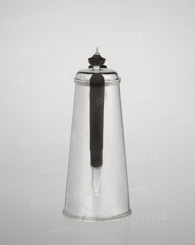 Conical coffee pot with hinged lid, slightly arched and flattened at the top, topped with a wooden handle made; short spout on axis with two sleeves for attaching a wooden handle added contemporarily. Engraved monogram tied HH beneath a ducal mitre; inscribed/dated 1890/1891. Maker: Barnard, Edward & Sons Ltd London; goldsmiths; active ca. 1680– ; also associated with Clark, Alfred Ltd London; goldsmiths and sellers; active 1898–1934. Materials: silver with wooden handle. Function: coffee ware. Place: London, England, Great Britain. Dimensions: height 17.3 cm, width 11 cm, depth 8.4 cm; weight 627 g., A tall conical metal container with a reflective silver surface and a dark vertical handle running down its front; the container has a rounded lid topped with a small decorative finial that combines silver and dark material, and a narrow spout extending from the handle area; the background is a smooth light gray gradient and the visible colors are silver, dark brown or black, and shades o...