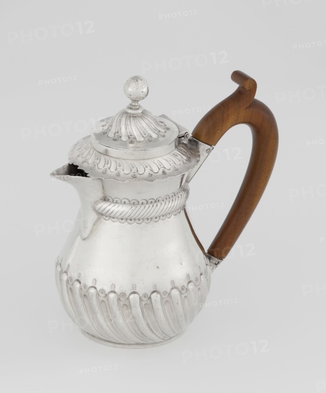 Coffee pot by John Septimus Beresford London; goldsmith's firm; active 1880–89. Pear-shaped jug, lower part spirally fluted, smooth above, decorated with a half-cylinder beneath the upper flared rim; short spout, wooden handle mounted in sleeves not original, hinged domed lid, spirally knotted, topped with a ball. 1888–1889. Great Britain — England, London. Vessel. Height 13 cm, width 12 cm, depth 6.8 cm, weight 179 g., A silver pitcher with ornate embossed patterns and a rounded ribbed lower body sits against a light gray background, topped by a domed lid with a round finial and decorative scalloped edges, and featuring a curved wooden handle in brown attached to the metal body; visible colors include silver, brown, and light gray.