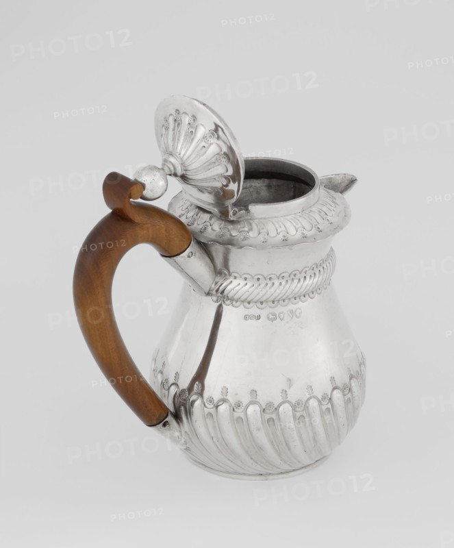 Coffee pot by John Septimus Beresford London goldsmith, active 1880–89. Pear-shaped jug, spirally clacked in the lower part, smooth above, decorated with a half-cylinder under the upper flared rim; short spout-shaped spout; wooden handle not original mounted in sleeves; hinged domed lid, spirally knotted, topped with a ball. Dated 1888–1889, Great Britain — England, London. Vessel. Height 13 cm, width 12 cm, depth 6.8 cm, weight 179 g., A metal pitcher with a curved wooden handle attached to its side, the metal surface is shiny and reflective with ornate fluted and scalloped decorative ridges around the body and rim, a hinged domed lid with embossed fan-like pattern is open and connected near the handle, the interior of the pitcher appears darker, and visible colors include silver on the metal and brown on the wooden handle, set against a light gray background.