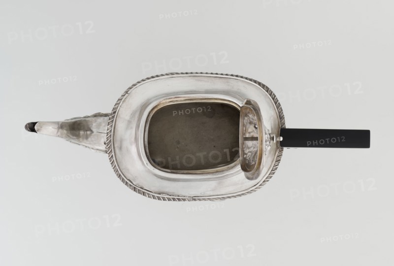 Teapot by Henry Moreton fl. 1899–1930s, factory owner and goldsmith; neo-Rococo style, silver, 1909–1910. Egg-shaped teapot on an oval plinth with a side spout, sleeves for attaching a wooden handle mounted on the axis, hinged centrally arched lid topped with a handle. Upper edge bordered with a band of godrons and a wide collar; decorated overall with neo-Rococo relief motifs and acanthus leaves, with an oval blind reserve on the belly framed by an acanthus rim. Function: tea vessel. Dimensions: height 13.5 cm, width 26 cm, depth 12 cm; weight 555 g. Place of origin: Chester, England., A metallic teapot is shown from above with a rounded rectangular body and an open lid revealing a hollow interior; the teapot has a decorative twisted rim and an elongated spout extending to one side, with a straight dark handle on the opposite side. The visible colors are silver tones on the metal, a dark gray interior, and black on the handle, all set against a pale neutral background.