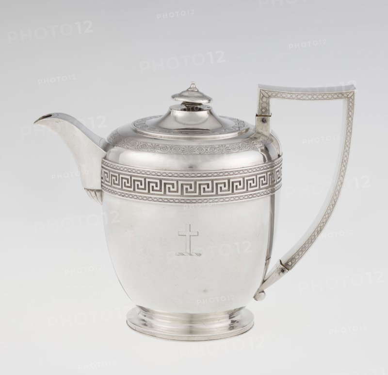 Teapot by John Emes fl. 1796–1808, goldsmith. Ovoid Georgian/George III teapot on a circular base with lid, c. 1806–1807, London, England. Decorated on the upper part of the belly with a wide band of meander ornament and braid. Ribbon-shaped, broken handle decorated with braid; high-set spout decorated at the base with a stylised palmette; lid finished with a knob-shaped finial. Engraved coat of arms on one side of the belly and a cross on the other. Materials: silver vessel. Dimensions: height 17.9 cm, width 23.7 cm; weight 815 g. Style: Empire/Georgian., A polished metal teapot with a reflective silver surface, featuring a curved spout on one side and a tall angular handle on the other, a domed lid with a small finial on top, a decorative band with a geometric pattern around the upper body, an engraved simple cross motif on the front, a rounded base, and a plain light gray to white background; visible colors include silver, gray, and white.