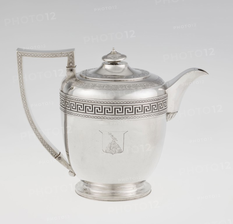 Teapot by John Emes fl. 1796–1808, English silver, c. 1806–1807. Ovoid teapot on a circular base with lid; decorated on the upper part of the belly with a wide band of meander ornament and braid. Side handle ribbon-shaped and broken in design, decorated with braid. Spout set high, decorated at the base with a stylised palmette. Lid finished with a knob-shaped handle. Belly engraved with a coat of arms on one side and a cross on the other. Empire/George III/Georgian style. Materials/technique: silver; function: tea vessel. Dimensions: height 17.9 cm, width 23.7 cm; weight 815 g. Made in London, England., A polished metal teapot with a curved spout and a tall angular handle sits against a light gray background; the body is rounded with a slightly stepped circular base and a domed lid topped by a small finial. The teapot surface shows an engraved band of geometric and braided patterns around the upper rim and decorative engraving on the lid and handle, and a simple engraved emblem on the ...