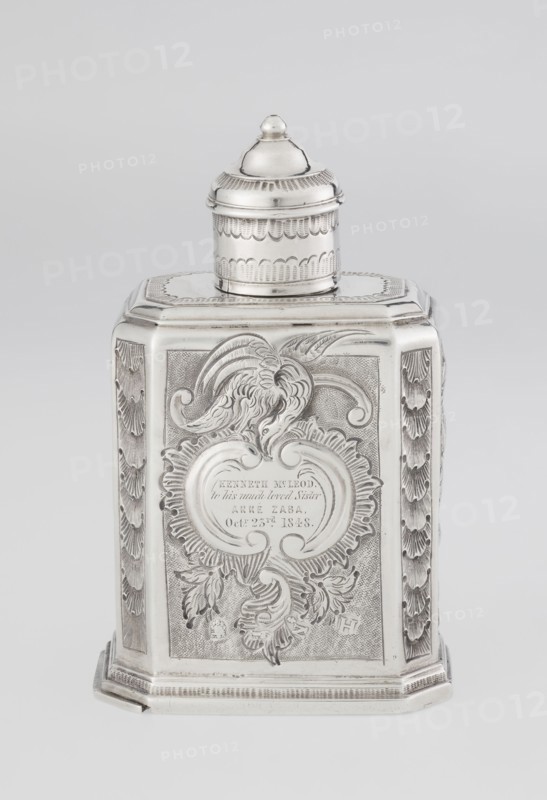 Tea caddy, Nash, Bowles fl. 1720–ca.1725 goldsmith; rococo; tea accessory; rocaille and floral roses, flowers ornament. Cuboid tea caddy with circular domed lid and a bowl on top; chamfered side edges; movable slide-in bottom. Surface decorated with repoussé floral and rocaille motifs on a grained background; front with an oval rocaille cartouche topped by an eagle, engraved inscription inside: KENNETH Mc LEOD, / to his much loved Sister / ANNE ZABA, / Octr 23 rd 1848; back wall with a bouquet of flowers; side walls with blooming, leafy roses. Engraved A on the bottom. Dated 1723/1724 tins; mid-19th century decoration. Place of origin: London, England. Vessel. Height 12 cm; width 7.7 cm; depth 5.7 cm; weight ca. 230 g., A silver-colored metal container with a rectangular base and a domed, removable lid sits against a light gray background. The main body has ornate engraved and embossed decoration including flowing acanthus-like foliage, curved cartouche shapes, and textured panels on t...