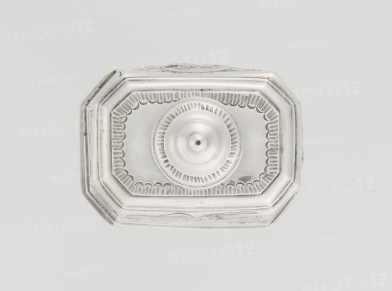 Tea caddy, Nash, Bowles fl. 1720–ca. 1725 goldsmith; rococo style; tea accessory; rocaille ornament, roses and flowers ornament; purchase provenance; dedications. Cuboid tea caddy with a circular domed lid and a bowl on the top; chamfered side edges; movable slide-in bottom. Surface decorated with repoussé floral and rocaille motifs on a grained background; front with an oval rocaille cartouche topped with an eagle and an engraved inscription inside: KENNETH Mc LEOD, / to his much loved Sister / ANNE ZABA, / Octr 23 rd 1848; back with a bouquet of flowers; side walls with blooming, leafy roses. Engraved A on the bottom; 1723/1724 tins; ca. mid-19th century decoration; England, London; vessel. Height 12 cm, width 7.7 cm, depth 5.7 cm, weight ca. 230 g., A top-down view of an octagonal metallic object with a raised central circular dome and decorative engraved border, showing a scalloped inner pattern and concentric ring detailing; the object appears silver in color with subtle darker gr...