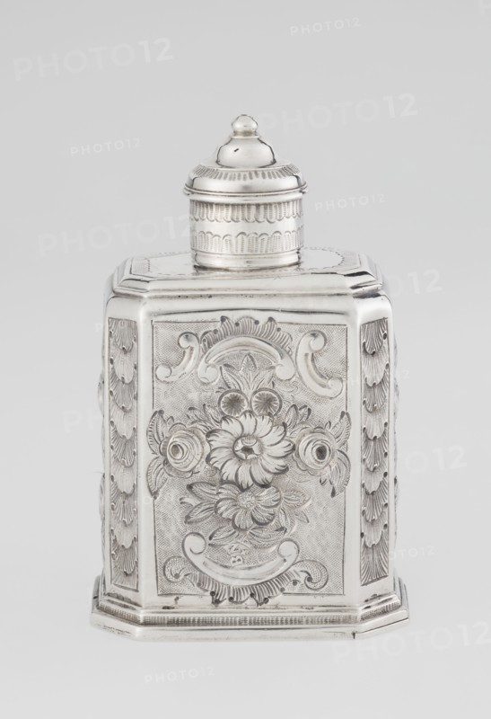 Tea caddy, Nash, Bowles fl. 1720–ca. 1725 goldsmith; rococo; tea accessory; cuboid tea caddy with circular domed lid and a bowl on top; chamfered side edges; movable slide-in bottom. Surface decorated with repoussé ornament of floral and rocaille motifs on a grained background; front features an oval rocaille cartouche topped with an eagle, with engraved inscription inside: KENNETH Mc LEOD, / to his much loved Sister / ANNE ZABA, / Oct 23rd 1848; back shows a bouquet of flowers; sides show blooming, leafy roses. Engraved S on the bottom; 1723/1724 tins; ca. mid-19th century decoration. London, England, Great Britain. Vessel. Height 12 cm; width 7.7 cm; depth 5.7 cm; weight ca. 230 g., A silver-colored metal container with a removable lid sits against a light gray background, showing an octagonal or multi-sided shape with ornate engraved floral and scrollwork designs on its front and sides; the lid is domed with concentric decorative bands and a small rounded finial on top, and the body...