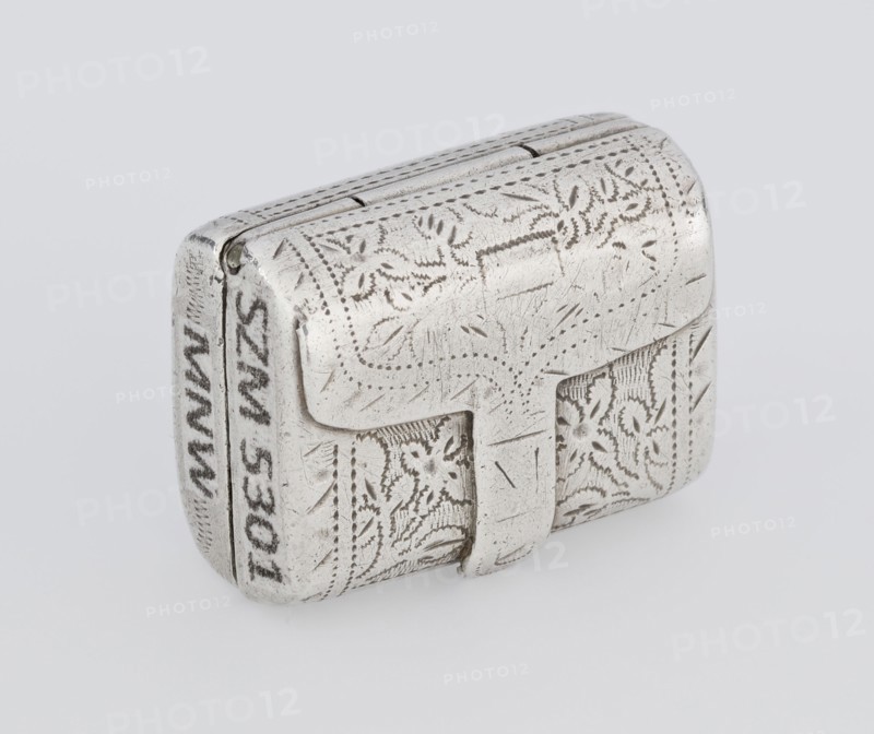 Fragrance container vinaigrette, 1834/1835. Silver vinaigrette in the form of a bag with an envelope closure and a protruding tongue, decorated on the front with dot-engraved flowers and leaves. Hinged lid opens to reveal an openwork insert decorated with plant scrolls. Engraved, bag shape; toilet accessory. Maker: Thomas Shaw fl. 1822–ca. 1840; 1782–1845. Birmingham, England. Height 2.1 cm; width 1.5 cm; depth 1 cm; weight 10 g., A small rectangular metal box with rounded edges sits against a light gray background; the box is silver in color with visible areas of darker tarnish and fine scratches, and its surface is covered in engraved floral and dotted decorative patterns. There is a hinged lid with a protruding clasp on the front, and the engraved motifs include leaf-like shapes and small curved details. The metal shows a mix of bright silver and duller gray tones, with some areas appearing slightly darker where the engraving and wear are deepest.