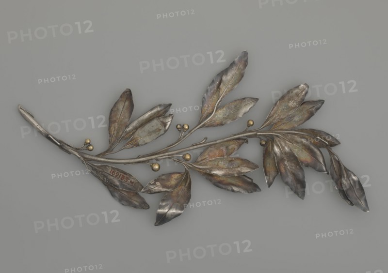 Laurel branch; creator, Paderewski, Ignacy Jan 1860–1941; end of 19th century; unknown locality; varia; height 29.7 cm; width 14.5 cm; weight 105 g, A metallic branch-like object with a group of elongated leaves and small spherical buds rests against a plain neutral background; the leaves show a range of colors including silver, gray, brown, greenish and subtle iridescent tones, and the small round buds are a golden color, while the background is a uniform light gray.