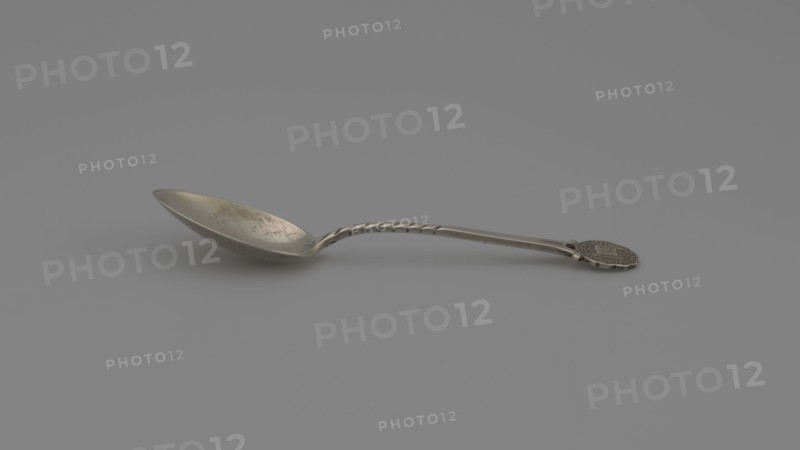 Souvenir spoon, Ford Company fl. 1875–1899 role classification of creator, goldsmith's company author, Paderewski, Ignacy Jan 1860–1941 — Souvenir spoon with an ovoid scoop with a pointed tip; half-handle with oblique notches, then flat, splitting at the end with a mounted circular plaque with a struck facsimile of the seal of Yale University in New Haven — in the center an open book with the Hebrew inscription URIM./TUMMIM enclosed in a cartouche around which is the Latin inscription LUX ET VERITAS motto; inscription around the rim: SIGILL: COLL: YALEN: NOV: PORT: NOV: ANGL:, 1890s, United States of America, New Haven, cutlery, height 10.5 cm, width 2.4 cm, weight 15 g, A metal spoon lying on a smooth gray surface, with a long twisted handle and a shallow bowl showing some mottled darker spots; the spoon and surface are shades of silver and gray, with subtle darker gray shadows beneath the spoon and a hint of brownish tarnish on the bowl.