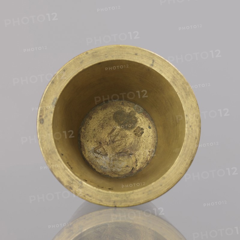Gwicht, unknown creator; Szewczykowski, Roman 1849–1901 — ; measures and weights; object in the shape of a truncated cone with markings: 4 M engraved inside and on the side 76; weight 935.18 g; end of 18th century; Germany; height 6.2 cm, width 8.6 cm, A top-down view of a cylindrical metallic cup with a golden-brass color, showing the interior with visible wear, scratches, and darker tarnished spots; the rim has concentric ridges and the inner walls are smooth with slight discoloration; the bottom interior shows mottled areas and textured marks; the object is reflected faintly on a glossy surface beneath, and the background is a muted light gray.