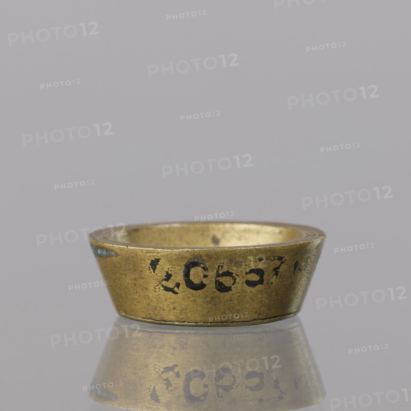 Gwicht; creator, Szewczykowski, Roman 1849–1901 associated name. In the shape of a truncated cone, marked inside 1. Weight 12.8 g. 18th century, Europe; Germany, Berlin. Height 0.9 cm; width 2.6 cm., A small metallic ring-shaped object with a flared outer edge sits on a reflective surface, showing a mirrored reflection beneath it; the object is primarily gold in color with areas of darker wear and a few spots of blue-green discoloration, and the background is a uniform light gray.