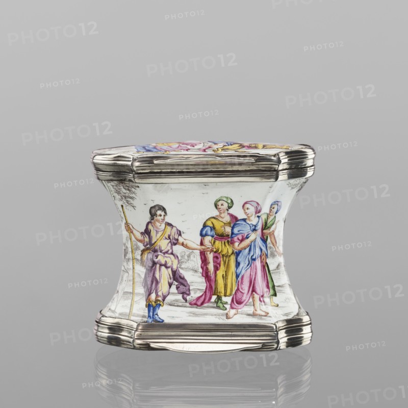 Double snuffbox, enameller LZ France?; fl. ca. 1700. Double-sided snuffbox, tall, narrowed halfway up; slightly bulging lids, framed by silver with profiled fittings. White-enameled, decorated with colourful scenes from the story of Samson depicted against a landscape painted in grisailles. Sides: Samson going to the Philistine city of Timna, shown the way by three women, and Samson fighting a lion. Lids: Samson carrying the door the city gate to the top of the mountain opposite Hebron and Samson taking honey from the lion's mouth. Reverses of the lids: two landscapes with architecture painted in grisailles and colourful flowers painted in the bottoms. Early 18th century France?, enamelling; smoking accessory. Height 7 cm; width 7.7 cm; depth 4.7 cm., A small decorative box with a curving hourglass-like profile and shiny metallic rims, shown resting on a reflective surface. The main body is white with a painted scene of a few figures in historical dress: one figure on the left holds a ...