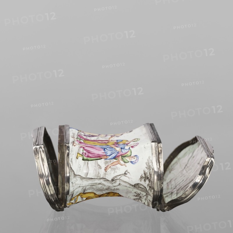Double snuffbox, enameller LZ France?; fl. ca. 1700. Double-sided snuffbox, tall, narrowed halfway up; slightly bulging lids, framed by silver, profiled fittings. White-enameled, decorated with colourful scenes from the story of Samson depicted against a landscape painted in grisailles. On the sides: Samson going to the Philistine city of Timna, shown the way by three women, and Samson fighting a lion. On the lids: Samson carrying the door the city gate to the top of the mountain opposite Hebron, and Samson taking honey from the lion's mouth. On the reverse of the lids: two landscapes with architecture painted in grisailles and colourful flowers painted in the bottoms. Early 18th century France?, enamelling; subject: Samson Bible — Samson fighting a lion; Samson collecting honey from a lion's mouth. Function: smoking accessory. Dimensions: height 7 cm, width 7.7 cm, depth 4.7 cm., An object with a curved, hourglass-like central section flanked by hinged lids, primarily white with hand-...