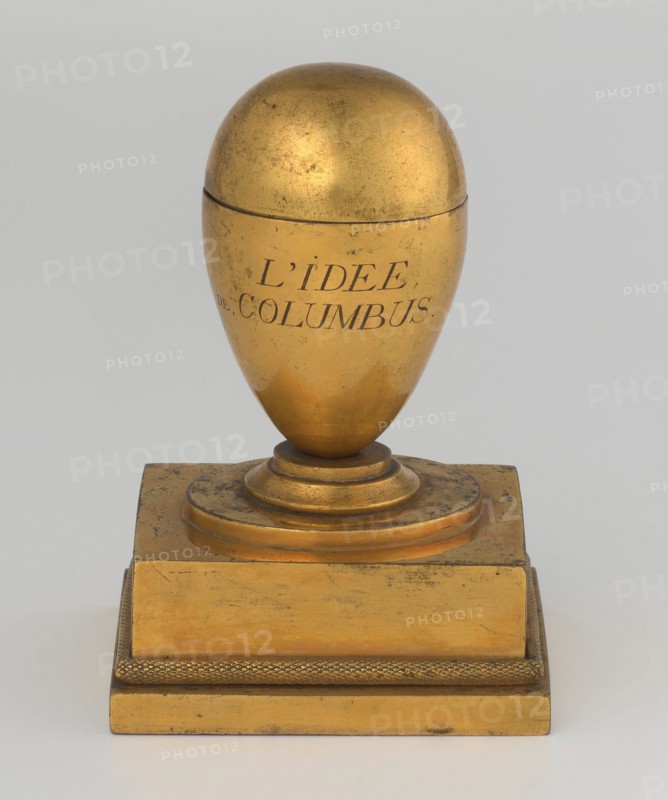 Inkwell, Tadeusz Bylewski 1866–1939, early 19th century, France, inkwell; height 13.5 cm, width 9.4 cm, depth 8.4 cm, A gold-colored ornamental object shaped like an egg on a stepped rectangular base, with a dome-like top and a rounded lower portion showing some surface wear and darker spots; the base and stepped platform share the same gold color and show areas of scuffing and darker discoloration, with a textured band around the lower edge of the platform; the background is a pale gray.