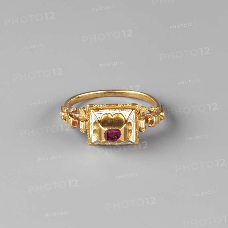 Renaissance ring, Renaissance style, body adornment hand adornment. Rectangular setting with a high box and a tabular-cut ruby, decorated with white enamel. Prism-shaped base with engraved hearts, on two side surfaces. Ring widens towards the base with solid volutes, decorated with opaque white, light blue, green, and red enamel. 2nd half of the 16th century, Central Europe. Jewelry. Height 2.2 cm, width 2.7 cm, depth 0.9 cm, weight 4.82 g., A gold ring with a square decorative top featuring a raised heart-shaped motif and a central round purple gemstone, a few small purple stones set near the band, and visible gold and white metal detailing against a light gray background.