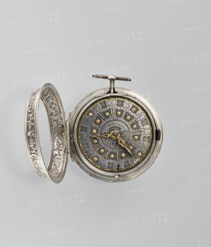 Pocket watch by Joseph Zeidlmayr fl. 1st half of the 18th century. Watch in a double case; outer case with a frame surrounding the dial and a repoussé depiction of the Crucifixion with Mary and St. John on the back, surrounded by a border of eight C-shaped sections and ornamental decoration. Smooth silver inner case; silver dial with Roman numerals for hours separated by gold dots and Arabic minute numerals. The reserve bears the signature of the watchmaker Zeidlmayr. Inside, the movement cover has a cutout revealing a bun. Movement marked: Breslau / Joseph Zeidlmayr. Inside the case: a negative MS mark, a negative mark and a possible illegible goldsmith's mark rosette?, and two numbers—markings likely made by repairing watchmakers. 1st half of the 18th century; Wroclaw Breslau, Silesia; timepiece., A round metal pocket watch with its decorated cover open, showing an ornate circular face with a patinated metallic surface and a range of metallic tones including silver, grey, dull gold, ...
