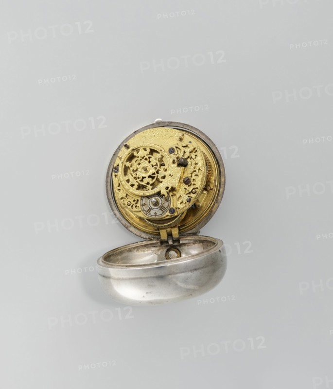 Pocket watch by Joseph Zeidlmayr fl. first half of the 18th century. Watch in a double case: outer case with a framed dial and a repoussé depiction of the Crucifixion with Mary and St. John on the back, surrounded by a border of eight C-shaped sections and ornamental decoration. Smooth silver inner case; silver dial with Roman numerals for hours separated by gold dots and Arabic minute numerals. The reserve bears the signature of the watchmaker Zeidlmayr. Inside, the movement cover has a cutout revealing a bun. The movement is marked Breslau / Joseph Zeidlmayr. Inside the case are a negative MS mark, a negative mark and a possible illegible goldsmith's mark rosette?, plus two numbers—markings likely made by repair watchmakers. Date: first half of the 18th century. Place of origin: Silesia Wroclaw. Type: timepiece., A small open pocket watch with an exposed ornate inner mechanism sits against a pale gray background; the watch case is metallic silver with a slightly worn surface and the ...