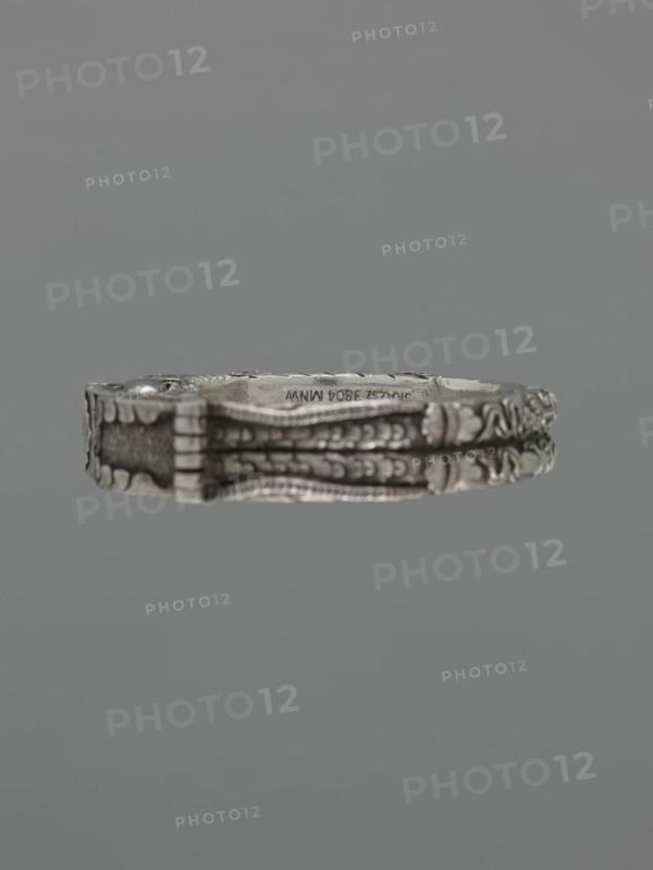 Bracelet, scrap - purchase, purchase provenance; Chinese and Mongolian art; body/hand ornament, fashion accessory; motif: dragon with pearl, hundred antiquities/baigu ornament; Chinese culture; 19th century ; place of origin: China, Mongolia ; material: jewelry; dimensions: height 8.0 cm, width 9.0 cm; weight 281 g., A close-up of a decorative metallic bracelet suspended against a solid gray background, showing ornate embossed patterns and raised detailing along its band with a mix of silver and darker gray tones and subtle darker shadows in the recessed areas.