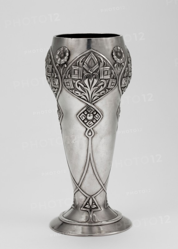 Art Nouveau vase, Khlebnikov goldsmith's workshop; 1840–1918, goldsmith. Scrap - purchase, purchase provenance. Art Nouveau style, geometric-floral ornament. Vase supported on a circular foot transitioning into a conical body, decorated with interlacing ribbons forming rhomboid reserves with geometric-floral decoration. Dated 1896–1908, Moscow, Russia. Vessel. Height 18.5 cm; width 8.1 cm; depth 7.8 cm; weight 322 g., A tall ornamental metal vase with a polished silver-gray surface standing against a light gray background, featuring ornate raised floral and geometric relief designs around its upper portion and along its shaft, with stylized flower motifs and curved leaf-like patterns, a flared rounded base with banded rims, smooth midsection contrasting with the detailed embellishments, and overall tones of silver, gray, and subtle darker gray shading.