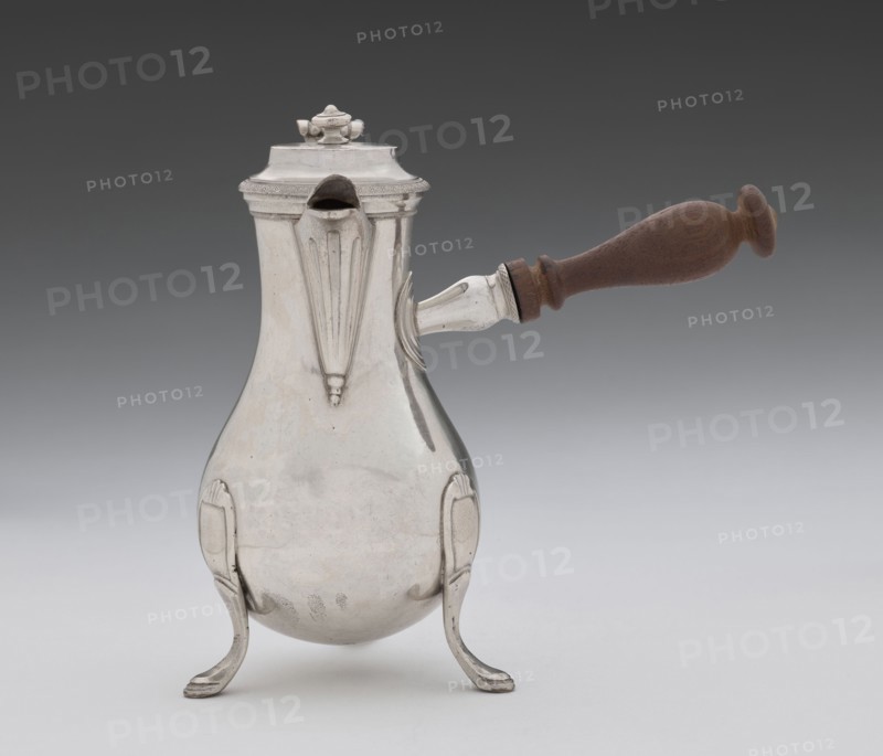 Coffee pot by Picard, F. fl. ca. 1798–ca. 1809. Silver vessel coffee pot, height 46.0 cm, width 8.5 cm, depth 8.5 cm, weight 248.2 g. Made in Paris, France, 1798–1809. Classified as tableware/coffee pot; associated with jugs and tableware items., A pear-shaped metal pot with a polished silver surface rests on a group of curved silver legs, featuring decorative vertical ridges and a spout near the top; a wooden handle with a warm brown color projects horizontally from one side, attached by a silver fitting, and a domed lid with a small ornamental finial tops the pot. The visible colors are silver, brown, and shades of gray in the background.