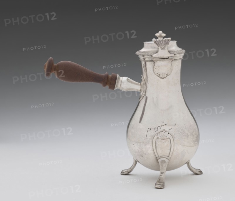 Coffee pot by F. Picard fl. ca. 1798–ca. 1809. Silver coffee pot, height 46.0 cm, width 8.5 cm, depth 8.5 cm, weight 248.2 g. Origin: Paris, France. Date: 1798–1809. Function: vessel coffee pot. Classification: tableware, jugs/coffee pots., A reflective metal pot with a bulbous body and a hinged lid stands on a group of curved legs; it has a dark brown wooden handle extending from one side with a turned shape, and the metal shows areas of light silver and subtle darker tarnish.