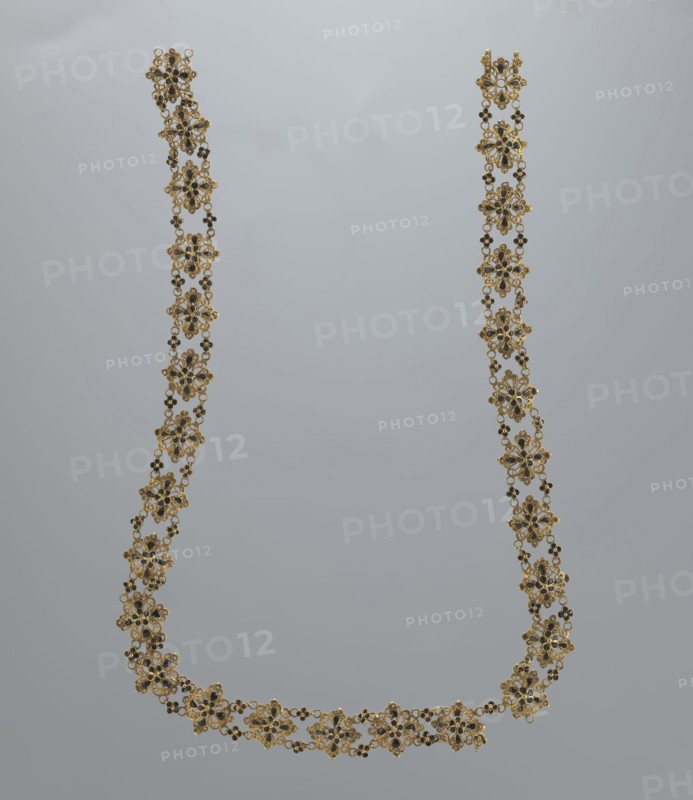Necklace, rosette motif, jewelry, women's accessory, mid-19th century, Italy, weight 16.57 g, length 37.5 cm, A delicate floral necklace suspended against a neutral gray background, composed of a repeating pattern of ornate flower-shaped links with filigree details, small round bead accents, and tiny connecting chains; the piece shows metallic gold tones with dark accents and subtle reflective highlights, forming a U-shaped drape with a few slight bends where it hangs.