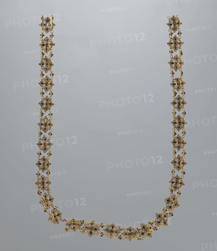 Necklace, rosette iconographic, jewelry, women's accessories, mid-19th century, Italy, weight 16.57 g, length 37.5 cm, A delicate gold necklace composed of a linked series of floral-shaped motifs forming a long U-shape against a pale gray background, each motif featuring small dark accents at the centers and tiny connecting loops, the gold showing warm yellow tones and the accents appearing deep brown to black, the overall composition presenting an ornate, lacy appearance with a few curved sections at the bottom and symmetrical vertical strands rising to matching clasps at the top.