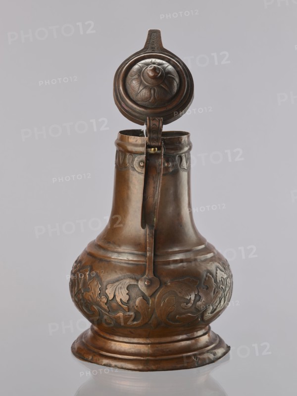 Jug. On a circular, stepped base, the body bulges in the lower part, decorated with a repoussé leafy twig and, at the rim, an eagle with spread wings. Above the two stepped areas is a neck with a spout. Repoussé leaves under the rim and along the rim. The hemispherical handle is fastened with rivets; the lid is hinged with a finger grip, arched, decorated with a leafy rosette and topped with a ball. Maker: Roman Szewczykowski 1849–1901 attributed/unknown role. 1st half of the 18th century, Poland. Vessel. Height 39.5 cm; width 23.9 cm; depth 28.4 cm., A metal pitcher with a hinged lid is shown against a plain light gray background; the pitcher has a rounded base that tapers into a narrow neck with a handle running from the lid to the body. The surface of the pitcher is a warm brownish-bronze with darker brown areas and subtle greenish patina in places, and it features raised decorative floral and foliate patterns around the bulbous midsection and a band of simple ornament near the top....