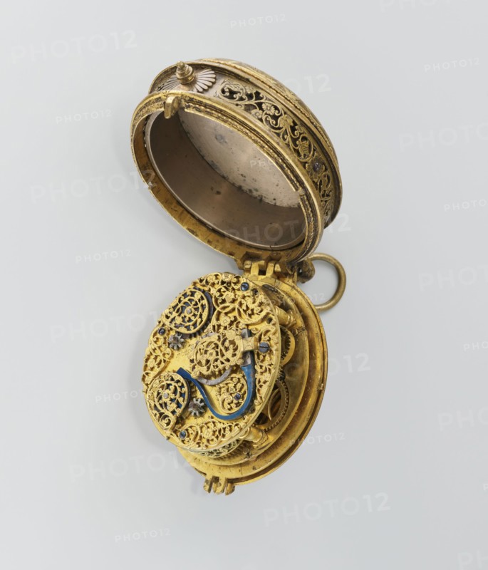Pectoral watch, Stosch, Israel fl. 1st half of 17th century watchmaker, baroque, floral ornament, grotesques. Pectoral watch in an oval case, frame with a circular glazed cut-out, beneath which a dial with a silver ring with hour numerals. Frame decorated with an engraved tendril. Underside open-work, with a motif of a winged bust passing at the bottom into a tendril; around it a tendril motif. Openwork sides of the case with a tendril motif. Mechanism with a striking device, signed I. STOSCH. 17th century; timepiece. Height 5.3 cm, width 3.5 cm., An open ornate circular metal object with intricate filigree work, showing a hinged lid and inner mechanical components; the object appears primarily gold with accents of blue and small dark elements, set against a light gray background.