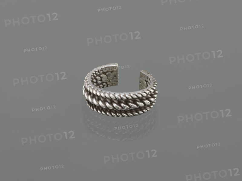 Bracelet; maker, 19th century, Middle East, Islamic art; body/female/hand ornament, fashion accessory; tugra motif; materials: jewelry unspecified; height 2.5 cm, width 7.0 cm, weight 170 g., A metallic ring with an open gap sits on a smooth surface, showing a braided rope-like texture around its exterior and a dotted, hammered pattern on its inner faces; the ring and its reflection display shades of silver and gray against a uniform gray background.