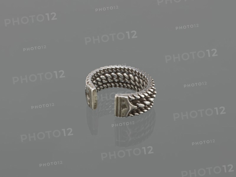 Bracelet, 19th century, Middle East, Islamic art; body/female/hand ornament, fashion accessory; tugra motif; materials: jewelry; dimensions: height 2.5 cm, width 7.0 cm, weight 170 g., A metallic open ring with a woven, braided texture forming its band, displaying a silvery-gray sheen and darker gray shadows, with two flattened end pieces that are slightly worn and show a variation of dull silver and gray tones against a uniform mid-gray background.