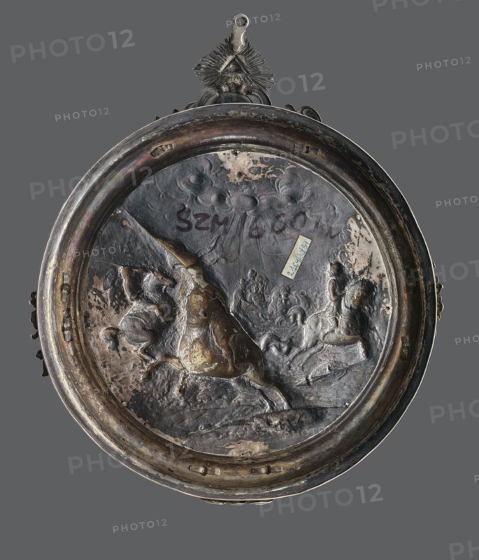 Plaque with a battle scene in a silver frame, Hardwald, Salomon fl. ca. 1700–ca. 1750 goldsmith frame, unknown goldsmith. Circular, repoussé, in parts in high relief, with a representation of an episode from the Thirty Years' War in a gilded circular profiled frame; on it four ungilded decorative elements; on the top, an oval plaque with the Slepowron coat of arms and the date 1752, above a pendant in the form of a triangular plaque with the Eye of Providence. The frame is marked on the edge with the iSHW Hardwald mark and 13. Attributed variously in older catalogues as Bavarian or Austrian work, 17th century/1752. Place associations: Poland, Warsaw, Netherlands. Plaque; height 26.5 cm, width 21.5 cm, weight 215 g., A round metal plaque with a raised rim and an attached decorative loop at the top, shown against a solid gray background; the plaque surface is a dark metallic color with areas of brownish and greenish patina and lighter worn patches, and the rim shows similar dark metallic...