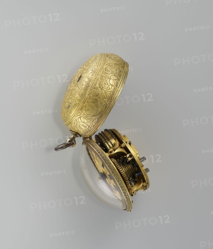 Pocket watch by Jacques Marcet fl. ca. 1725–ca. 1750, 2nd quarter of the 18th century. Gilded silver, almost spherical double case; enameled numerals on the dial. Cases decorated with plant decoration: inner case with flowers in a vase in a reserve formed by a ribbon that on the outer side forms heart-shaped loops with floral sprigs between them; a strip of plant-floral tendrils on the side of the case. Outer case has a flower sprig in a circular central reserve, surrounded by an interwoven ribbon and floral sprigs in the fields. Movement with openwork bow and Jacques/Marcet signature; inside both cases marked with number E. 4 unidentified. Engraved decoration stylized in a Middle Eastern style—possibly intended for the Turkish market. Possible French maker, though he may have worked in England if Huguenot. Timepiece; height 6.5 cm, width 5.5 cm, depth 4 cm., A decorative pocket watch case and partially exposed inner mechanism resting against a plain light gray background, the outer ca...