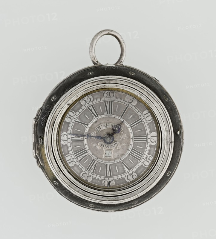 Pocket watch by John Bushman 1692–1720. Silver pocket watch in three cases: outer case covered with leather, rim decorated with studded silver rosettes; middle and inner cases plain. Underside of inner case stamped with casemaker's initial H and number 3081. Transparent lid. Silver champlevé dial with Roman numeral hour markers and Arabic minute markers in oval reserves on a matte background; central circular reserve with the watchmaker's signature on two semicircular plates reading BUSHMAN and LONDON; date window at the bottom. Steel hands with openwork hour hand. Movement with plate skeleton, spring drive, worm gear, and Gall chain; spindle escapement. Gilded lower plate with openwork English-style bun in the form of a wreath filled with acanthus tendrils and openwork grid, connected by a mascaron mask with an openwork bun foot. Hair adjustment is a rotating silver-plated dial with scale I–VI. Engraved on the plate in italics: Jn Bushman 3081 / LONDON. Circa 1700, London, England. Ti...