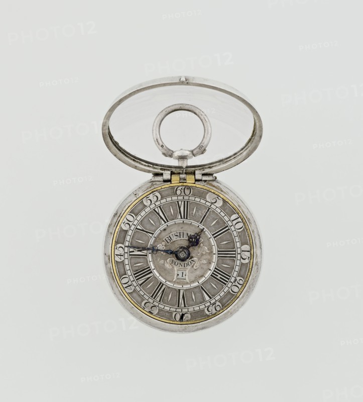 Pocket watch by John Bushman 1692–1720. Silver pocket watch in three cases: outer case covered with leather and decorated on the rim with studded silver rosettes; middle and inner cases plain. On the underside of the inner case the casemaker's initial H and the number 3081. Transparent lid. Silver champlevé dial with Roman numeral hour markers and Arabic minute markers in oval reserves on a matte background; central circular reserve with the watchmaker's signature in two semicircular plates reading BUSHMAN and LONDON; date window at the bottom. Steel hands with openwork hour hand. Movement with a plate skeleton, spring drive, worm gear, and Gall chain. Spindle escapement. Gilded lower plate with an openwork English-style bun in the form of a wreath filled with acanthus tendrils and an openwork grid, connected by a mascaron mask with an openwork bun foot. Hair adjustment as a rotating silver-plated dial with a scale I–VI. Engraved on the plate in italics: Jn Bushman 3081 / LONDON. Circa...