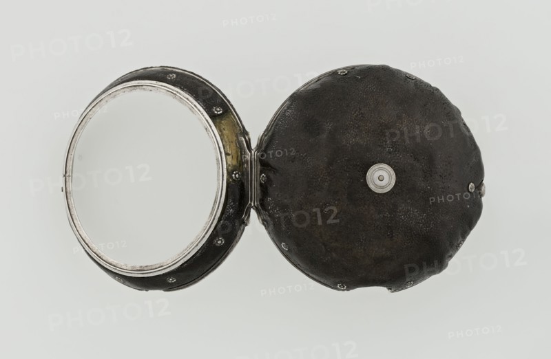 Pocket watch by John Bushman 1692–1720. Silver pocket watch in three cases: outer case covered with leather, rim decorated with studded silver rosettes; middle and inner cases plain. Underside of inner case engraved with casemaker's initial H and number 3081; transparent lid. Silver champlevé dial with Roman numeral hour markers and Arabic minute markers in oval reserves on a matte background; central circular reserve with the watchmaker's signature in two semicircular plates reading BUSHMAN and LONDON; date window at the bottom. Steel hands, openwork hour hand. Movement with plate skeleton, spring drive, worm gear, and Gall chain; spindle escapement. Gilded lower plate with an openwork English-style bun in the form of a wreath filled with acanthus tendrils and an openwork grid, connected by a mascaron mask with an openwork bun foot. Hair adjustment is a rotating silver-plated dial with scale I–VI. Engraved on the plate in italics: Jn Bushman 3081 / LONDON. Circa 1700, London, England....